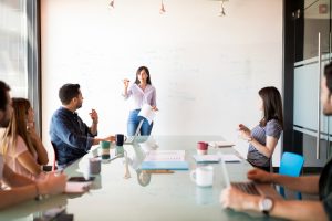 latina woman giving a presentation to a group around a table
